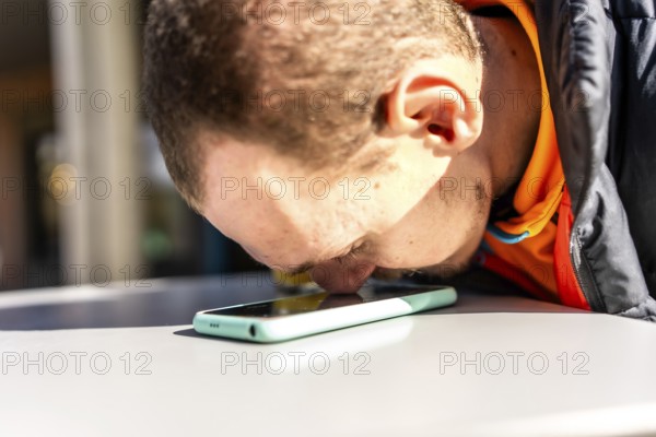 Young visually impaired man using assistive technology to interact with smartphone, touching the screen with his nose to navigate and communicate