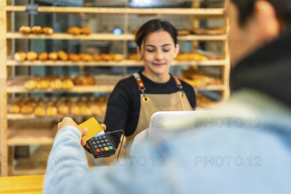 Rear view of a latin man paying with credit card and contact less terminal in an artisan bakery