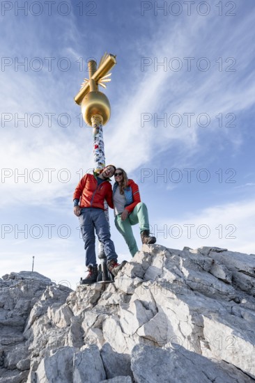 Couple, two mountaineers in front of a golden summit cross, summit of the Zugspitze, Wetterstein range, Bavaria, Germany, Europe
