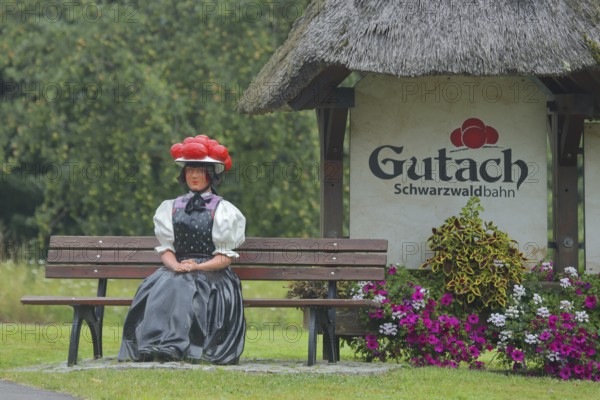 Doll in woman's traditional costume with Bollenhut on bench, Black Forest, Bollenhut, clothing, skirt, tradition, traditional, sitting, park bench, inscription, sculpture, floral decoration, Gutach-Black Forest railway, Ortenau, Southern Black Forest, Black Forest, Baden-Württemberg, Germany, Europe