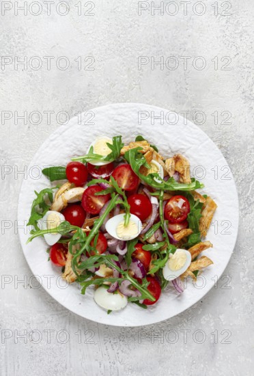 A warm salad with fried chicken fillet, arugula and cherry tomatoes, and boiled quail eggs, on a white plate, no people