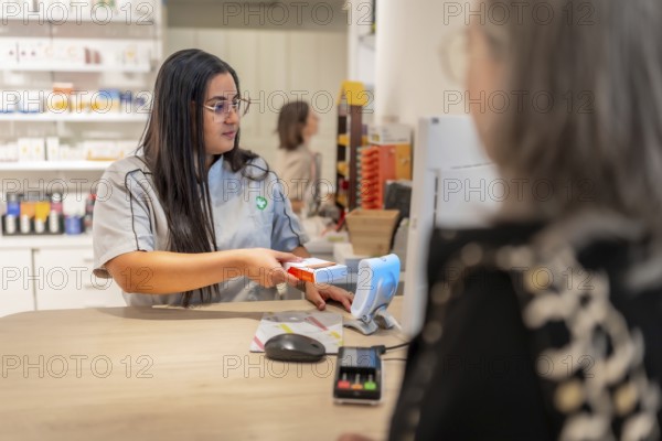 Pharmacist checking the price of a product attending a client in the counter of a modern pharmacy store
