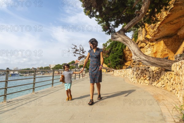 Mother and son enjoying a leisurely stroll along the scenic seaside promenade of puerto cristo, mallorca, spain