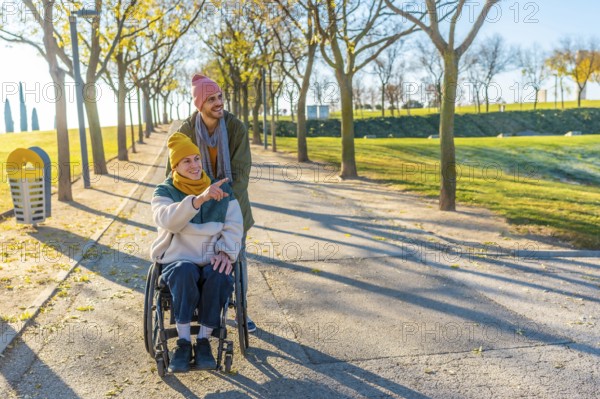 Happy friends enjoying a sunny autumn day together outdoors in a park, one pushing a wheelchair and the other pointing towards something