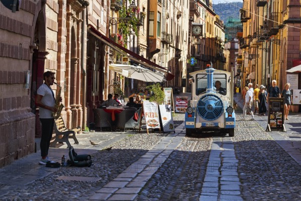 Trolleybus, street musicians, pedestrians and tourists in the picturesque old town of Bosa, Oristano, Western Sardinia, Sardinia, Italy, Europe