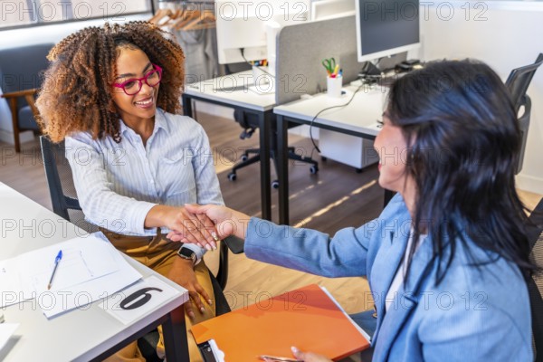 Two happy businesswomen shaking hands after a successful job interview in a modern coworking office