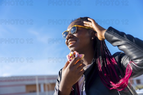 Low angle view photo of an african woman eating a multicolored doughnut in the street