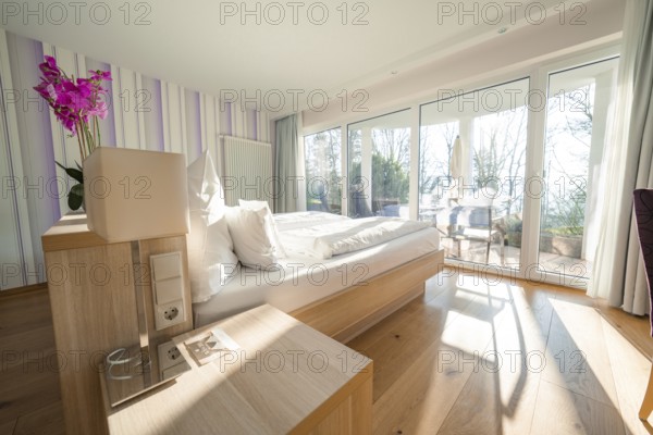 Modern, bright bedroom with wooden floor, large windows and a purple flower on the bedside table, Hotel Krone Lamm, Zavelstein, Black Forest, Germany, Europe