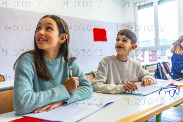Two young pupils listening to their teacher in elementary school classroom during lesson, education concept
