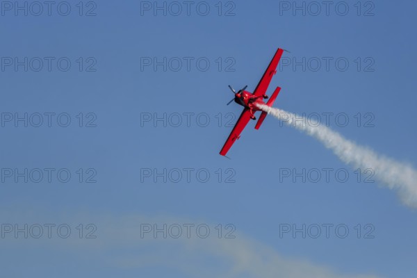 Red stunt aerobatic plane performing stunts in blue sky. Concept of speed, difficulty, precision, risk