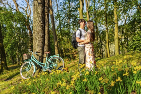 Romantic couple hugging in a forest full of daffodils with a bicycle parked nearby, enjoying a sunny spring day