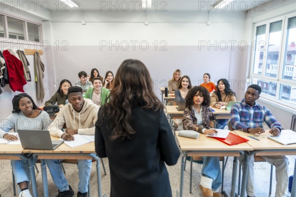 Female professor teaching a lesson to a multi ethnic group of students sitting at desks in a classroom
