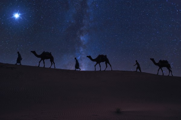 Christmas Jesus birth concept - Adoration of the Magi, Three Wise Men, Three Kings, and the Three biblical Magi with camel silhouettes journeying in sand dunes of desert follow Bethlehem star at night