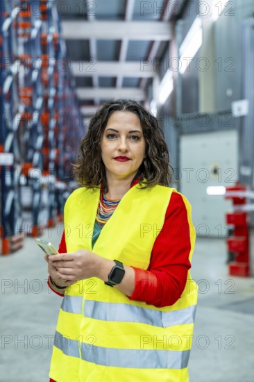 Vertical portrait of a female manager of warehouse wearing safety reflective clothes using mobile phone