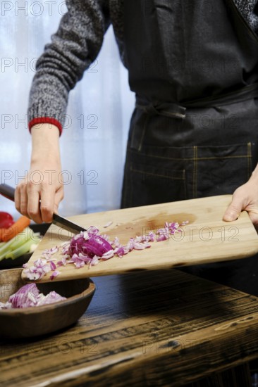 Unrecognizable man puts chopped red onions from a wooden cutting board in wooden bowl in the kitchen