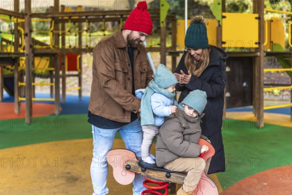 Parents watching their children joyfully riding a spring rider on a colorful playground, creating cherished memories and bonding together
