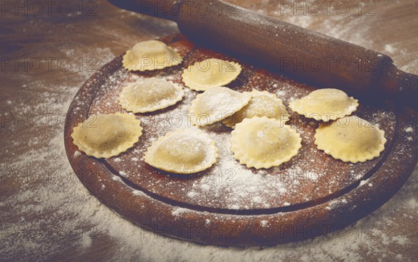 Fresh raw, uncooked ravioli, on a cutting board, with a rolling pin for dough, wooden background, no people