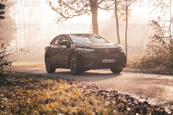 A Volkswagen on a country road in the morning sun mist between autumnal trees, electric car VW ID5, Deer Carsharing, Gechingen, Black Forest, Germany, Europe