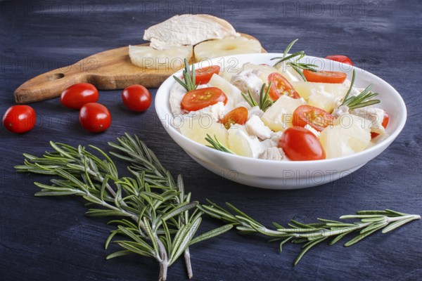 Chicken fillet salad with rosemary, pineapple and cherry tomatoes on dark blue wooden background. close up, copy space