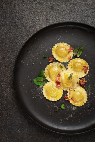 Fresh ravioli, with butter, spices and herbs, fried bacon, on a black plate, top view, dark background, no people