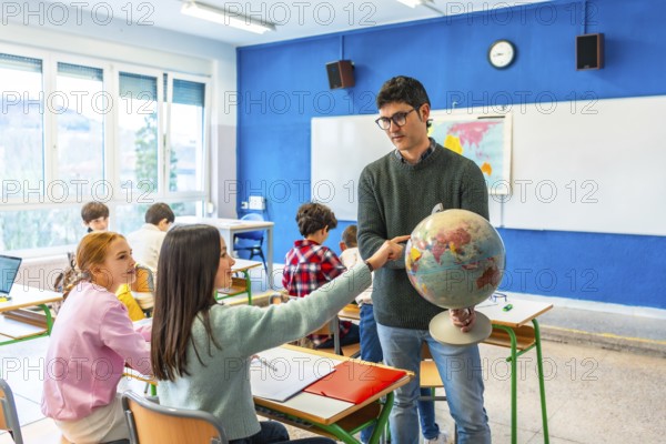 Geography teacher engaging students by pointing out countries on a globe during an interactive lesson in a lively classroom setting