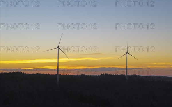 Two wind turbines in front of a glowing sunset sky over a wooded landscape, Baden-Württemberg, Germany, Europe