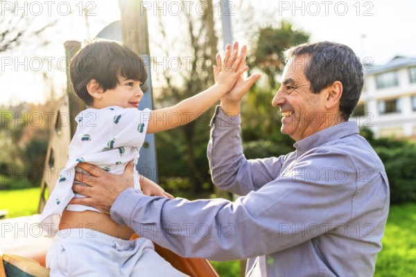Grandfather and grandson are enjoying time together at the playground, giving a high five and smiling