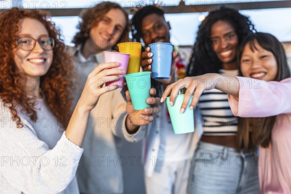 Frontal view of a group of young happy multi-ethnic friends toasting at camera celebrating in terrace