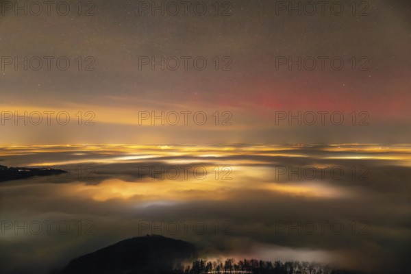 Firework lights under the sea of fog. New Year's Eve fireworks 2024 and a little red Aurora Borealis Northern Lights. On the Breitenstein, Swabian Alb near Ochsenwang. Sea of fog in the foothills of the Alb. View towards Stuttgart. In the foreground Hahnenkamm and on the left the Hörnle looks out of the fog