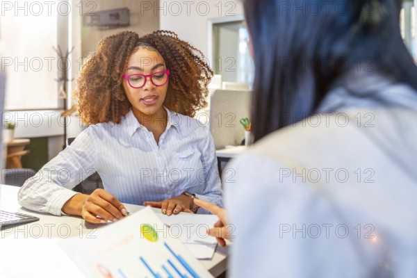 Two businesswomen analyzing financial charts and discussing company strategy in a modern coworking office
