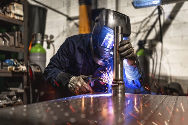 Concentrated male worker wearing protective gloves and facial mask welding in a metal factory alone
