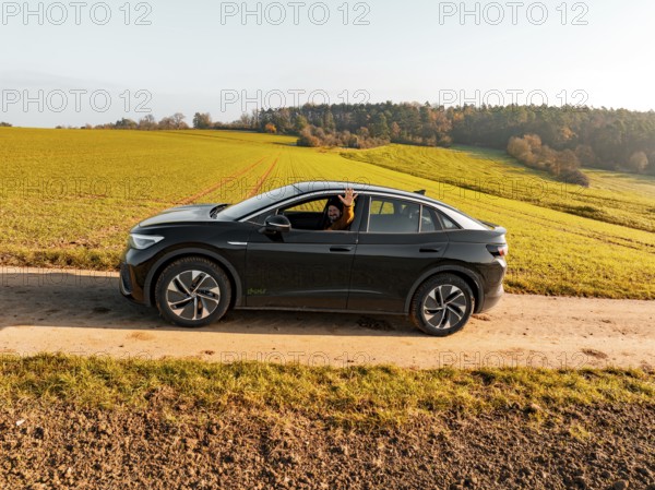 A driver sits in a black car on a dirt track, surrounded by green meadows, electric car VW ID5, Deer Carsharing, Gechingen, Black Forest, Germany, Europe