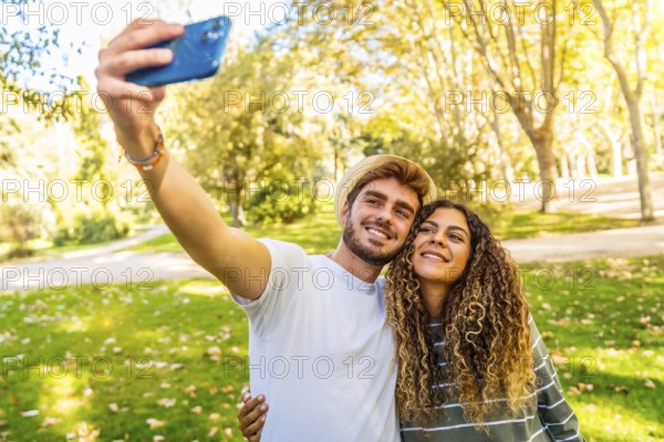 Frontal view of a young caucasian couple taking selfie standing in a park in a sunny day of spring