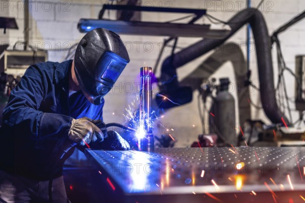 Unrecognizable man with safety goggles and gloves working in a factory welding pieces of metal