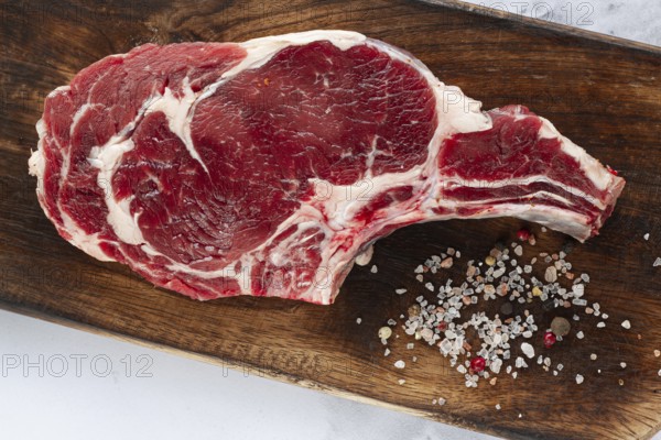 Raw rib eye steak, cowboy steak, wooden chopping board, marble table, top view, no people