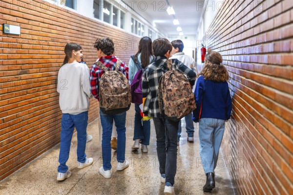 Rear view of diverse group of students walking down school hallway between classes, carrying backpacks and chatting