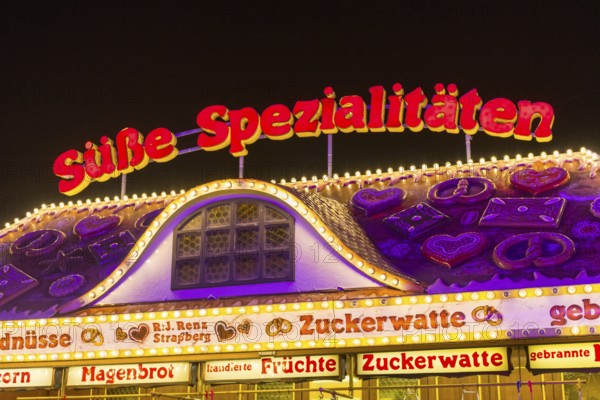 Candy stall flooded with light at a funfair at night, decorated with traditional treats, Cannstatter Wasen, folk festival, Bad Cannstatt, Stuttgart, Baden-Württemberg, Germany, Europe