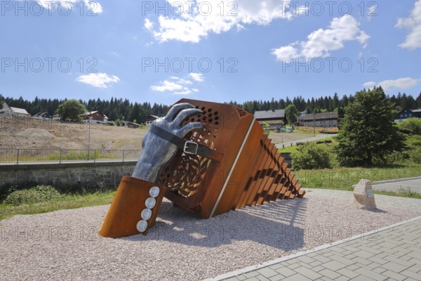 Sculpture bandoneon with hand, strap and buckle as a monument and symbol of musical instrument making, hand harmonica, hand-pull instrument, accordion, harmonica, oversize, oversized, rusty, sculpture, historical manufacture, production, industry, finger, strap, musical instrument, Carlsfeld, Eibenstock, Westerzgebirge, Erzgebirge, Saxony, Germany, Europe