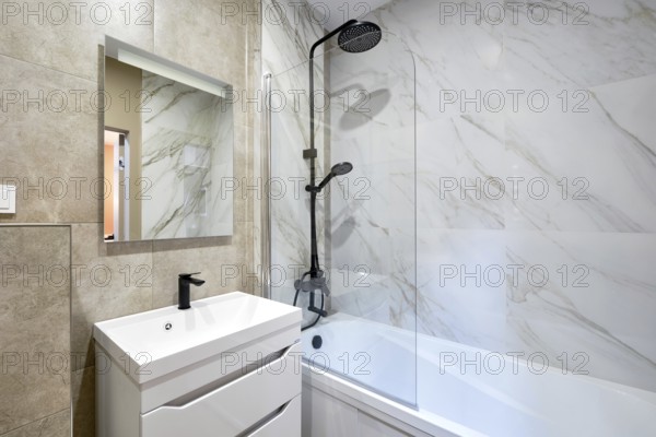 A beautifully designed bathroom showcases marble walls and a stylish shower-bathtub combo. A modern vanity with a mirror adds functionality and elegance to the space