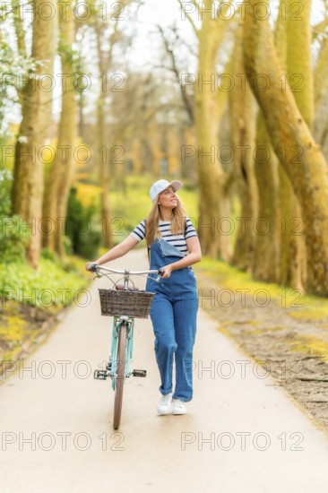 Young woman walking with her vintage bicycle in a beautiful tree lined path, enjoying a sunny autumn day outdoors
