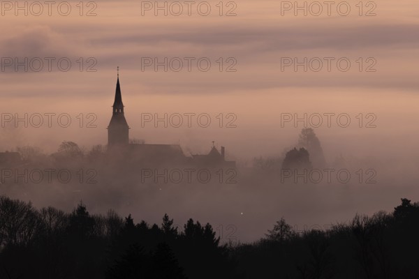 Wisps of mist drift into the town of Kronberg im Taunus in the morning shortly in front of sunrise. Only the spire of St Peter and Paul's Church stands out. Kronberg, Malerblick, Hesse, Germany, Europe