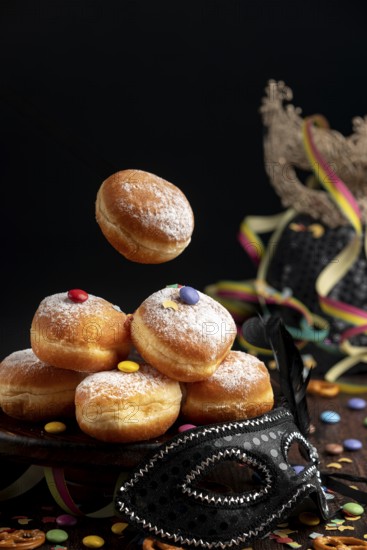 Berliners, doughnuts with icing sugar and Smarties next to a black mask, carnival