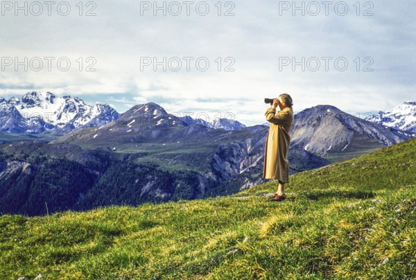 Woman standing on hillside using binoculars in mountains of national park, Western Rhaetian Alps, Switzerland, Europe 1959, Europe