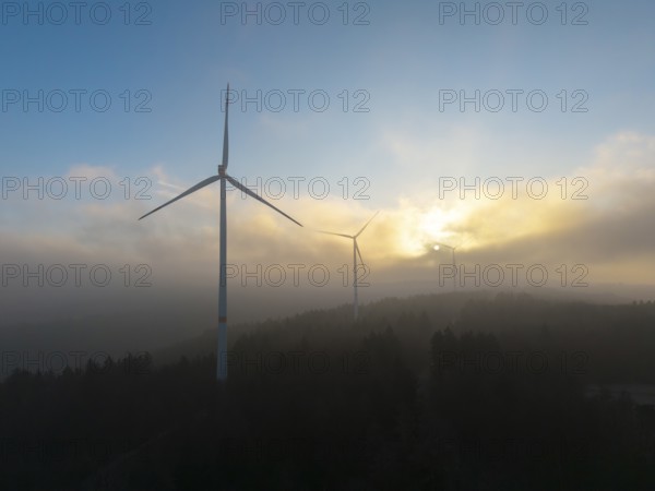 Wind turbines in the fog with the sun rising behind the trees, Rems Valley, Baden-Württemberg, Germany, Europe