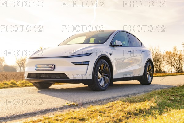 White electric car on a country road in sunny weather and open field, Tesla, New Model Y Juniper, Germany, Europe