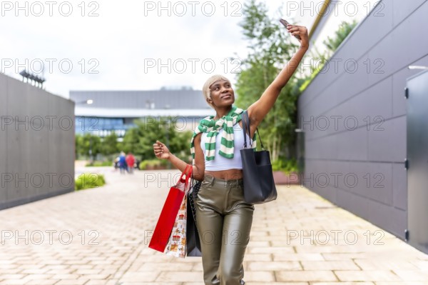 African woman carrying shopping bags taking selfie with cellphone outside a shopping mall
