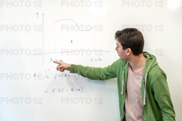 Young college student explaining a mathematical integral calculus formula, pointing at a graph on a whiteboard