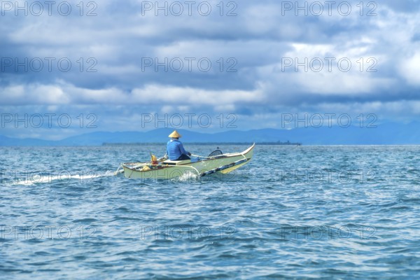 Traditional outrigger boat sailing on turquoise water with a fisherman wearing a straw hat, near the coast of siargao island