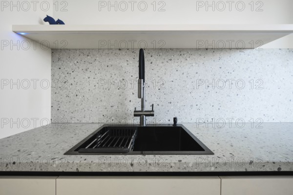 A sleek kitchen showcases a contemporary sink with a black finish, set against a light speckled countertop and minimalistic shelving for a stylish cooking space.