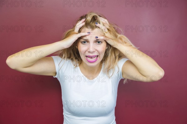 Concept of worry, woman with both hands on head on red background